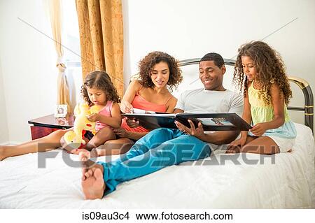 Family sitting on bed looking through photo album, looking down smiling View Large Photo Image Picture - Family sitting on bed looking through photo album, looking down smiling. Fotosearch