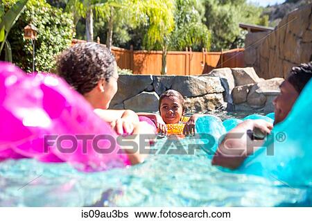 Stock Photograph - Family with girl in pool using inflatables talking. Fotosearch