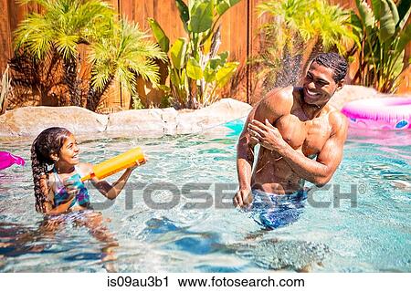 Stock Image - Father and daughter playing with water pistol in swimming pool. Fotosearch