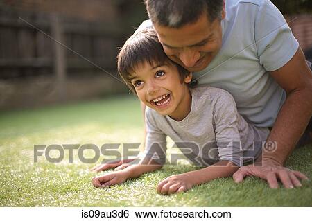 Stock Photograph - Father in garden lying on top of smiling boy. Fotosearch