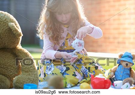 Stock Photograph - Girl having teddy bear picnic in garden pouring tea. Fotosearch