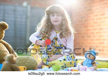 Stock Photography - Girl having teddy bear picnic in garden holding toy teacup. Fotosearch