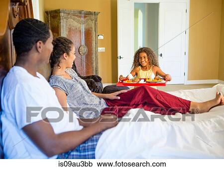 Stock Image - Girl serving parents breakfast in bed smiling. Fotosearch