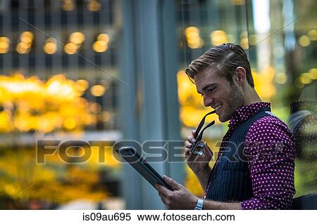 Happy young businessman leaning against park window reading digital tablet View Large Photo Image Stock Photography - Happy young businessman leaning against park window reading digital tablet. Fotosearch