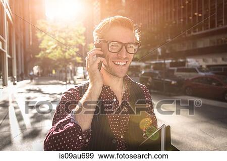 Stock Photo - Happy young businessman strolling city street talking on smartphone, New York, USA. Fotosearch