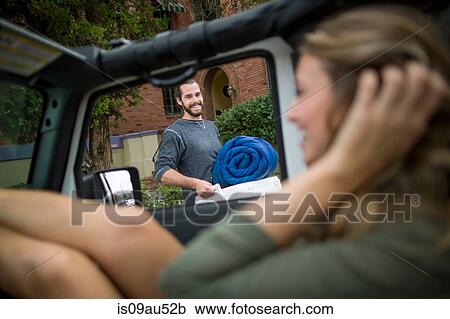 Stock Image - Happy young couple preparing jeep for road trip. Fotosearch
