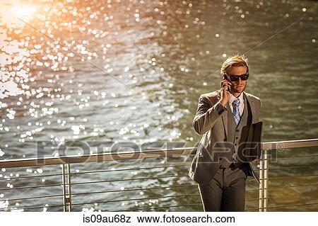 High angle view of young businessman talking on smartphone on city waterfront View Large Photo Image Stock Photo - High angle view of young businessman talking on smartphone on city waterfront. Fotosearch