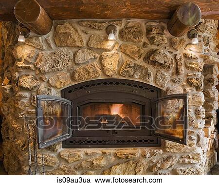 Lit Fieldstone And Rock Fireplace In Living Room In Cedar Log Home