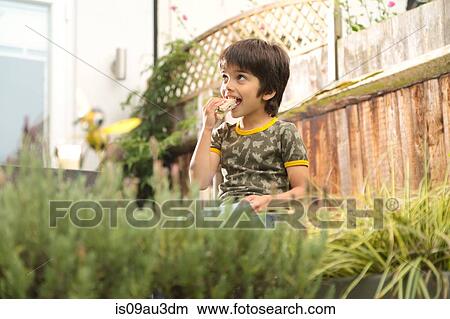 Low angle view of boy sitting in garden eating sandwich looking away View Large Photo Image Picture - Low angle view of boy sitting in garden eating sandwich looking away. Fotosearch