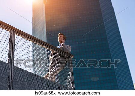 Low angle view of young businessman chatting on smartphone on city balcony, New York, USA View Large Photo Image Stock Photo - Low angle view of young businessman chatting on smartphone on city balcony, New York, USA. Fotosearch