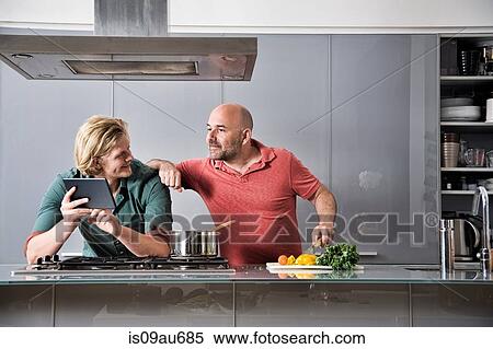 Male couple looking at digital tablet whilst preparing food in kitchen View Large Photo Image Stock Photography - Male couple looking at digital tablet whilst preparing food in kitchen. Fotosearch