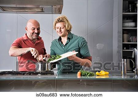 Stock Image - Male couple preparing food together in kitchen. Fotosearch