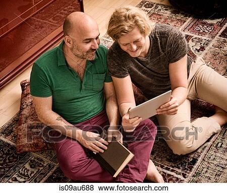 Male couple sitting on floor looking at digital tablet View Large Photo Image Stock Photo - Male couple sitting on floor looking at digital tablet. Fotosearch
