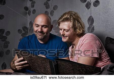 Stock Photograph - Male couple sitting up in bed looking at photo album. Fotosearch