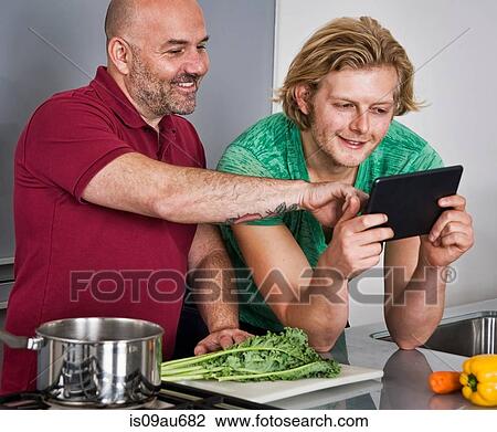 Male couple using digital tablet whilst preparing food in kitchen View Large Photo Image Stock Image - Male couple using digital tablet whilst preparing food in kitchen. Fotosearch