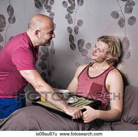Mature man handing breakfast in bed to boyfriend View Large Photo Image Stock Photograph - Mature man handing breakfast in bed to boyfriend. Fotosearch