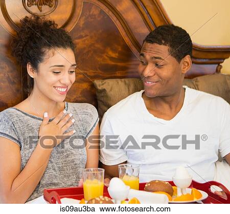Stock Image - Mid adult man surprising young woman with breakfast in bed. Fotosearch
