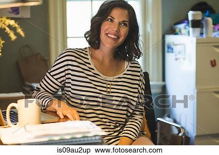 Stock Photography - Mid adult woman at desk, laptop and coffee cup in front of her, looking away. Fotosearch
