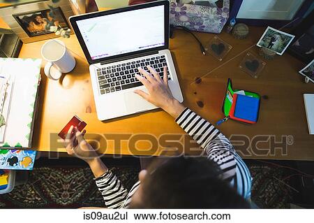 Mid adult woman at desk, using laptop, holding credit card, overhead view View Large Photo Image Stock Image - Mid adult woman at desk, using laptop, holding credit card, overhead view. Fotosearch