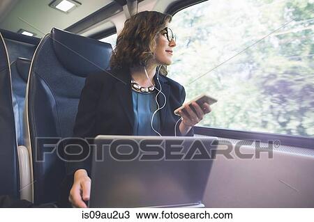 Mid adult woman on train, holding smartphone, laptop in front of her View Large Photo Image Stock Image - Mid adult woman on train, holding smartphone, laptop in front of her. Fotosearch