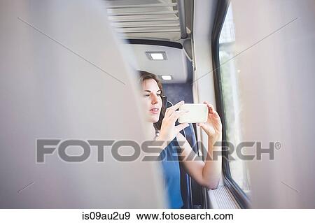Mid adult woman on train, taking photograph through window using smartphone View Large Photo Image Stock Photo - Mid adult woman on train, taking photograph through window using smartphone. Fotosearch