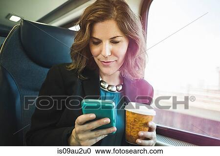 Mid adult woman on train, using smartphone, holding coffee cup View Large Photo Image Stock Image - Mid adult woman on train, using smartphone, holding coffee cup. Fotosearch