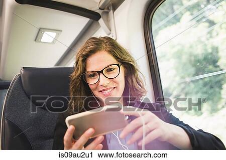 Mid adult woman on train, using smartphone, wearing earphones View Large Photo Image Stock Image - Mid adult woman on train, using smartphone, wearing earphones. Fotosearch