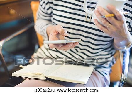 Mid adult woman sitting, holding smartphone and coffee cup, mid section View Large Photo Image Stock Photograph - Mid adult woman sitting, holding smartphone and coffee cup, mid section. Fotosearch