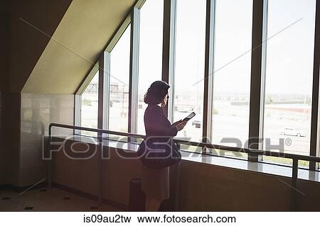 Stock Photo - Mid adult woman standing beside window, holding digital tablet. Fotosearch