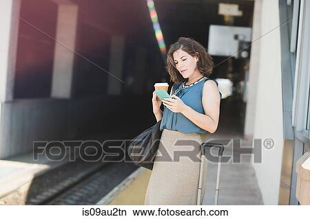 Mid adult woman waiting at train station, using smartphone, holding coffee cup View Large Photo Image Picture - Mid adult woman waiting at train station, using smartphone, holding coffee cup. Fotosearch