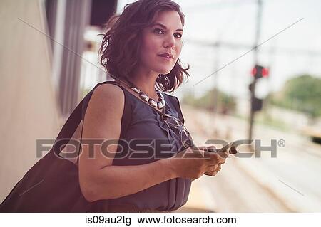 Mid adult woman waiting at train station, holding smartphone View Large Photo Image Stock Image - Mid adult woman waiting at train station, holding smartphone. Fotosearch