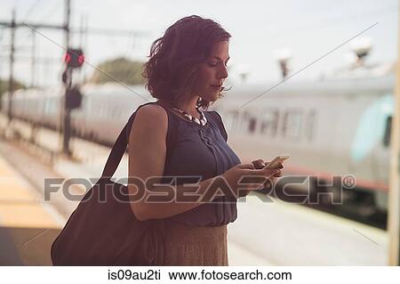 Mid adult woman waiting at train station, holding smartphone View Large Photo Image Stock Image - Mid adult woman waiting at train station, holding smartphone. Fotosearch