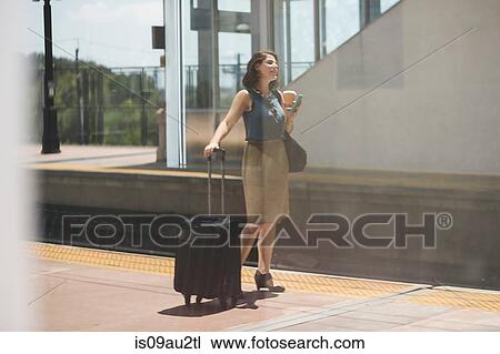 Mid adult woman waiting at train station, holding wheeled suitcase and coffee cup View Large Photo Image Stock Image - Mid adult woman waiting at train station, holding wheeled suitcase and coffee cup. Fotosearch