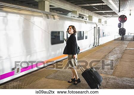 Mid adult woman waiting to board train, holding wheeled suitcase and smartphone View Large Photo Image Stock Photo - Mid adult woman waiting to board train, holding wheeled suitcase and smartphone. Fotosearch