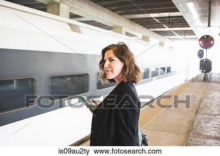Mid adult woman waiting to board train, holding smartphone View Large Photo Image Stock Photo - Mid adult woman waiting to board train, holding smartphone. Fotosearch