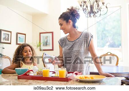 Stock Image - Mother and daughter at home preparing breakfast tray smiling. Fotosearch
