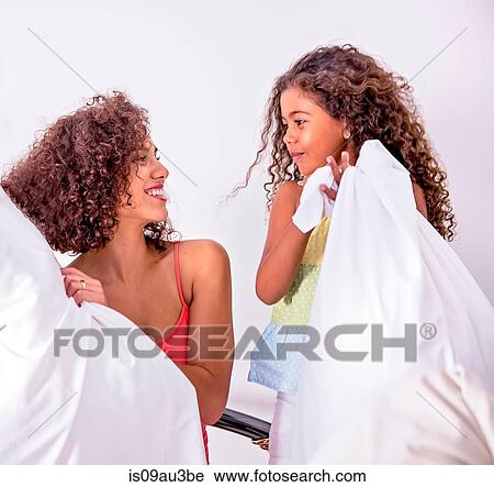 Stock Image - Mother and daughter holding pillows face to face smiling. Fotosearch