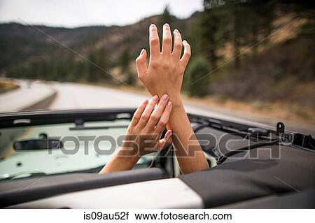 Stock Image - On the road view of young womans hands raised through jeep sunroof. Fotosearch