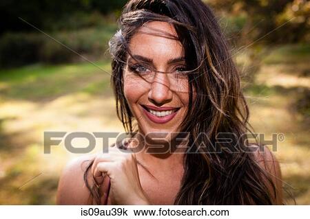 Stock Image - Portrait of bare shouldered mid adult woman with windblown hair looking at camera smiling. Fotosearch