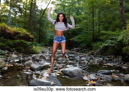 Stock Photography - Portrait of happy young woman jumping over forest river rocks. Fotosearch
