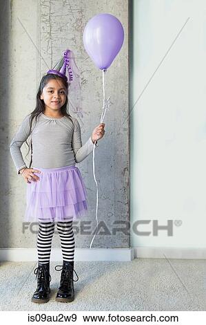 Stock Photo - Portrait of young girl, wearing party clothes, holding purple balloon. Fotosearch