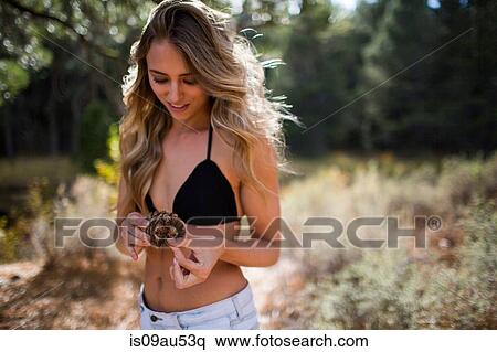 Stock Photography - Portrait of young woman in sunlit forest holding pine cone, Lake Tahoe, Nevada, USA. Fotosearch