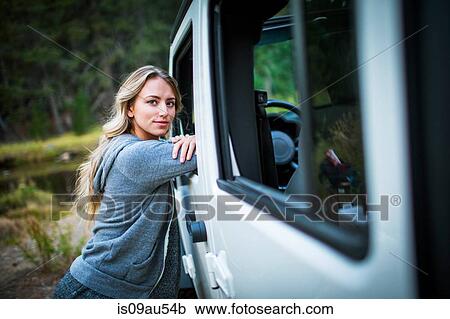 Stock Image - Portrait of young woman leaning against jeep at riverside, Lake Tahoe, Nevada, USA. Fotosearch