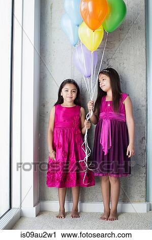 Stock Image - Portrait two young girls holding balloons. Fotosearch