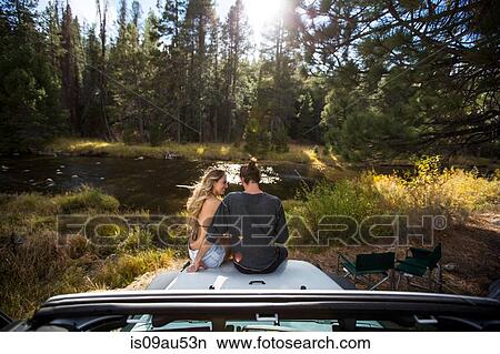 Picture - Rear view of romantic young couple sitting on jeep hood at riverside, Lake Tahoe, Nevada, USA. Fotosearch