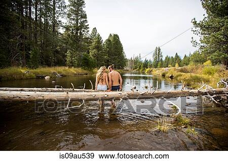 Stock Photo - Rear view of romantic young couple sitting on fallen tree in river, Lake Tahoe, Nevada, USA. Fotosearch