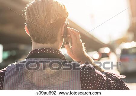 Rear view of young businessman talking on smartphone on city street View Large Photo Image Stock Image - Rear view of young businessman talking on smartphone on city street. Fotosearch