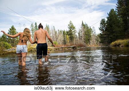Stock Image - Rear view of young couple crossing river, Lake Tahoe, Nevada, USA. Fotosearch
