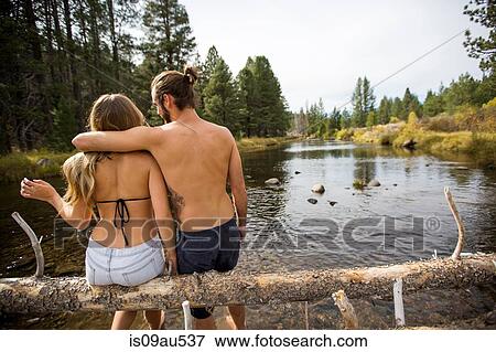 Rear view of young couple sitting on fallen tree in river, Lake Tahoe, Nevada, USA View Large Photo Image Stock Photo - Rear view of young couple sitting on fallen tree in river, Lake Tahoe, Nevada, USA. Fotosearch