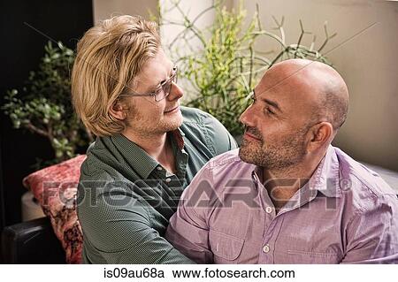 Stock Image - Romantic male couple looking at each other on sofa. Fotosearch